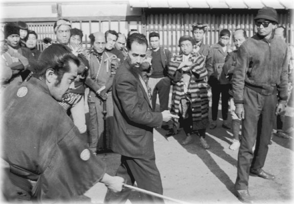 Master Sugino instructing famed actor Mifune Toshiro on the set of Yojimbo with legendary Director Akira Kurosawa (in hat and glasses) looking on